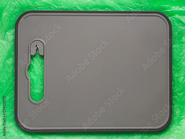 Fototapeta Gray plastic textured cutting board is on a crumpled plastic green background. Can be used as a backdrop for advertising. Flat lay. Copy space