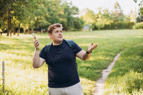 Obraz Sad blonde man got lost and could not find an internet connection on phone on the nature background. Male explorer looking for connection to the internet or using gps navigator app on phone