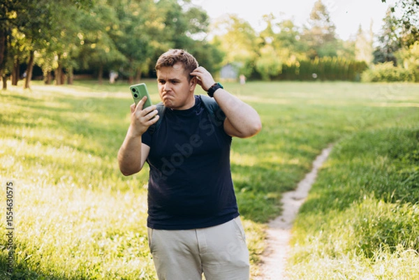 Obraz Sad blonde man got lost and could not find an internet connection on phone on the nature background. Male explorer looking for connection to the internet or using gps navigator app on phone
