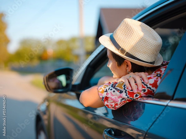 Fototapeta Traveler woman in red ethnic dress and hat drives car through scenic countryside of Croatia in summer. Surrounded by lush fields and forests, she enjoys peaceful and adventurous road trip