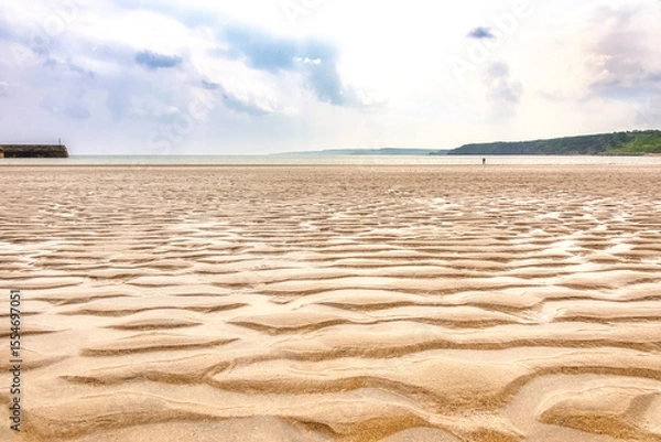 Fototapeta A sandy beach where a receding tide has left ripples of sand and puddles of water.