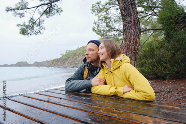 Fototapeta Couple enjoys Turkish coastline. Sitting on stones, watching sea waves, relaxing together, slow romantic moment near calm blue water under soft winter light.