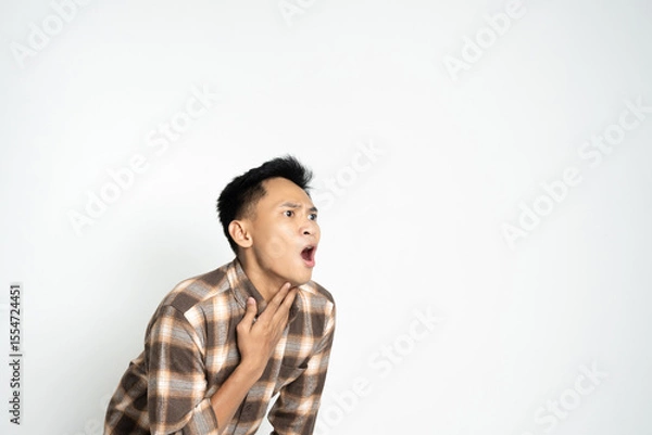 Fototapeta Asian young man dressed casually in a checked shirt touching his throat while looking concerned.