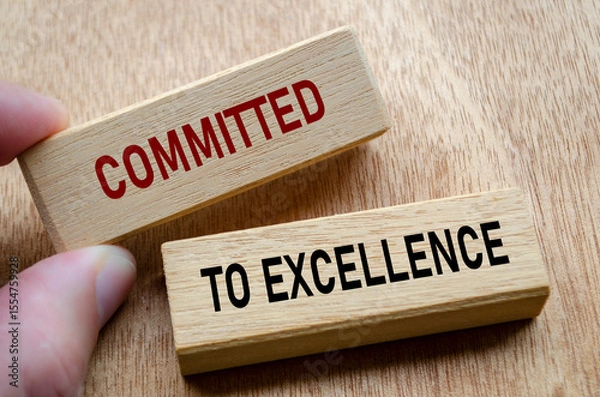 Fototapeta Fingers align wooden blocks that declare commitment to EXCELLENCE, reinforcing an unshakable focus on quality and continuous progress
