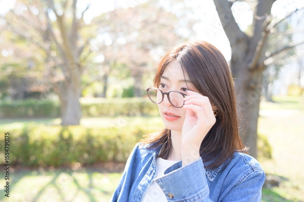 Fototapeta 眼鏡を持ち上げる仕草を見せながら春の空気の中で女性が穏やかに微笑む瞬間の自然光ポートレート