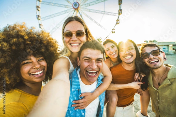 Fototapeta Multiracial group of friends taking selfie with smart mobile phone outside - Happy young people having fun in front of ferris wheel at summer vacation - Technology and summertime holidays concept