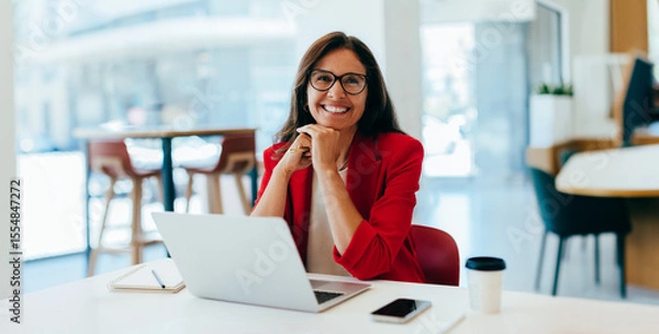 Fototapeta Confident businesswoman in red jacket smiling while working on a laptop