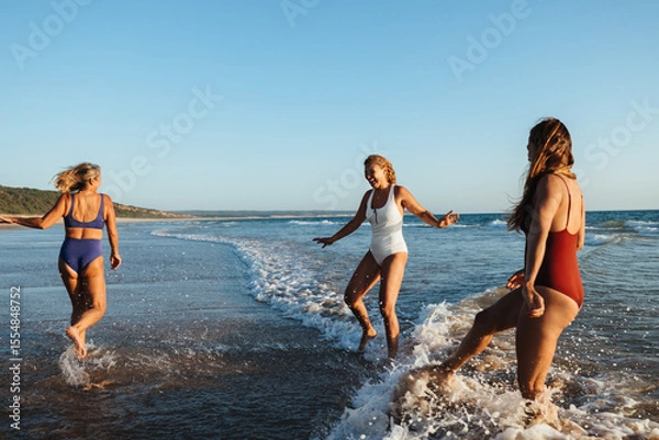 Fototapeta Three friends play joyfully in the ocean at a scenic beach.