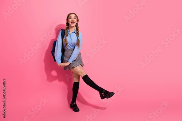 Fototapeta Happy young student girl in school uniform posing against pink background with a cheerful expression showcasing youth and style