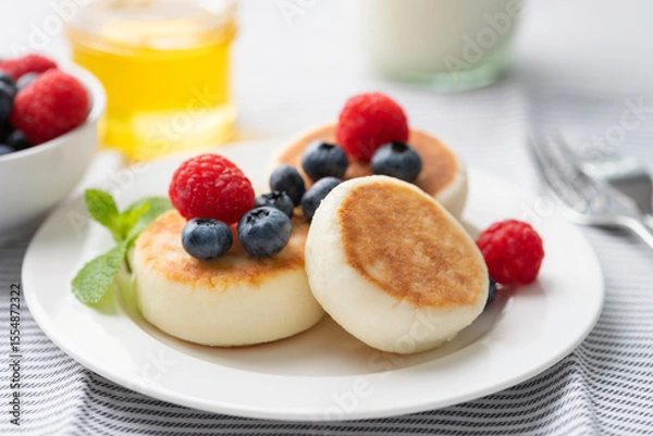 Fototapeta Cottage cheese fritters with berries and honey on a plate,closeup view