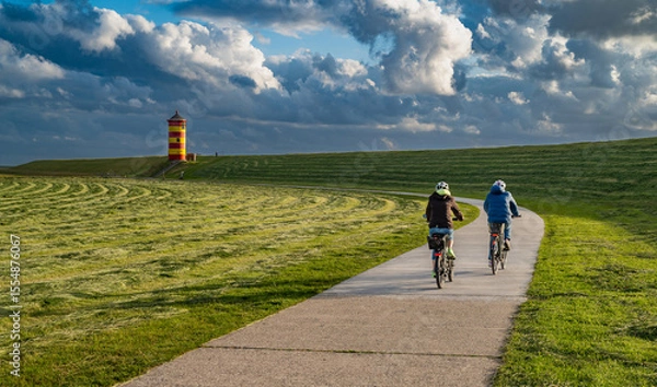 Obraz Radfahrer auf dem Weg zum Pilsumer Leuchtturm in Ostfriesland, Deutschland