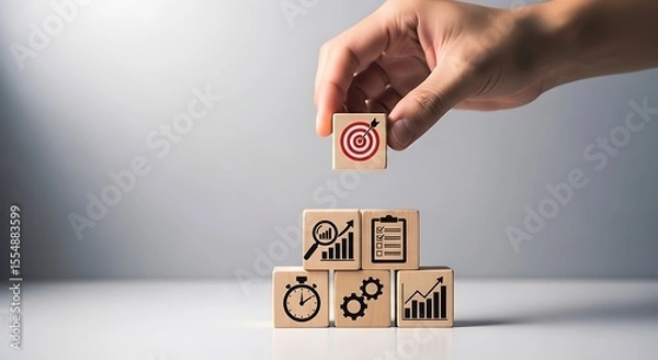 Obraz Hand placing wooden cube with target arrow on top of stacked cubes showing graphs checklist stopwatch and gears