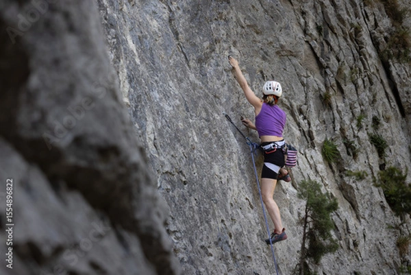 Obraz A woman is climbing a rock wall with a purple shirt and black shorts