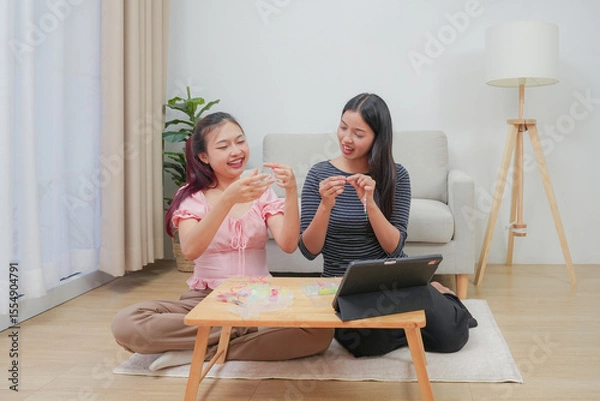 Fototapeta Two young asian women stringing beads on thread and choosing colorful beads from box to making handmade bracelet while spending time to creating jewelry handicraft and doing hobby lifestyle at home. 