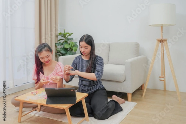 Fototapeta Two young asian women stringing beads on thread and choosing colorful beads from box to making handmade bracelet while spending time to creating jewelry handicraft and doing hobby lifestyle at home. 