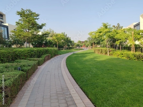 Obraz Small Interlock Path Between Landscaping Area.
Green And Lush Landscaping Area With Carpet Grass And Trees Like Palm Or Washingtonia, Some Houses Or Villa's Also Beside Gardens Padestrian Pathway.
