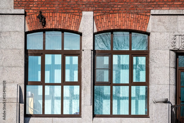 Fototapeta Two rectangular windows with a red brick arch against a grey block wall. From the Windows of the World series.