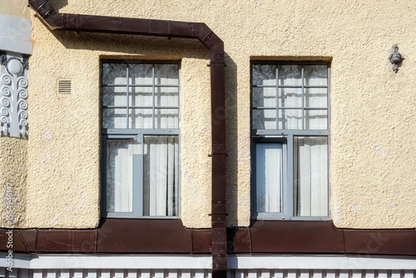 Fototapeta Two rectangular windows on a beige wall with a brown rectangular drainpipe. From the Windows of the World series.