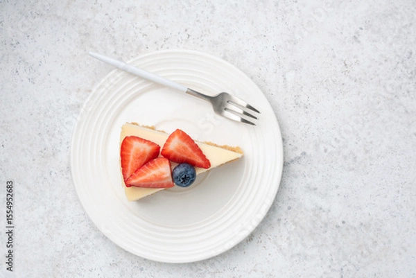 Fototapeta Slice of cheesecake with fresh berries topping on white plate, top view copy space for text, grey concrete background
