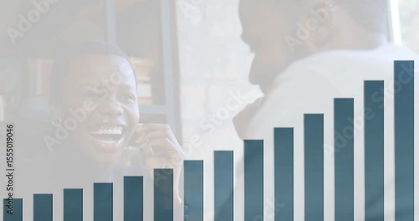 Obraz Laughing business professionals discussing sales figures at desk, with smartphone and bar chart
