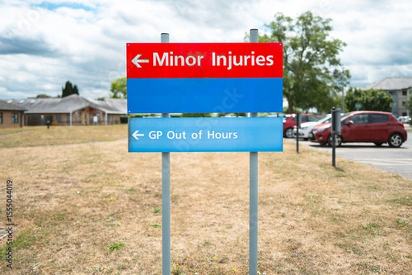 Fototapeta Typical Minor Injury sign seen together with an out of hours GP department at a typical NHS hospital in Britain. A patient car park is in the right, administration buildings in the distance.