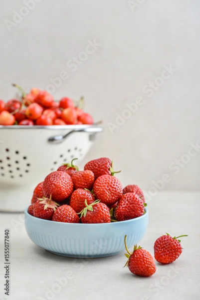 Fototapeta Ripe strawberries in a blue bowl and a white enamel colander full of sweet cherries