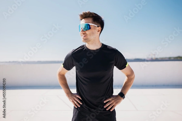 Fototapeta Runner enjoys a sunny day on an urban, showcasing athletic style and vibrant eyewear while preparing for an energetic workout