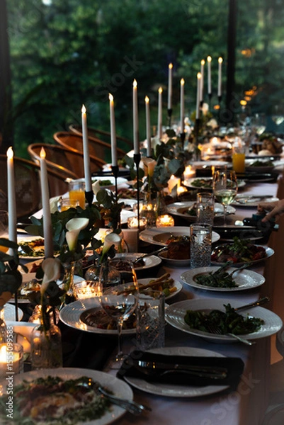 Obraz Elegant dinner table setting with candles and gourmet food ready for a celebration in a lush green environment