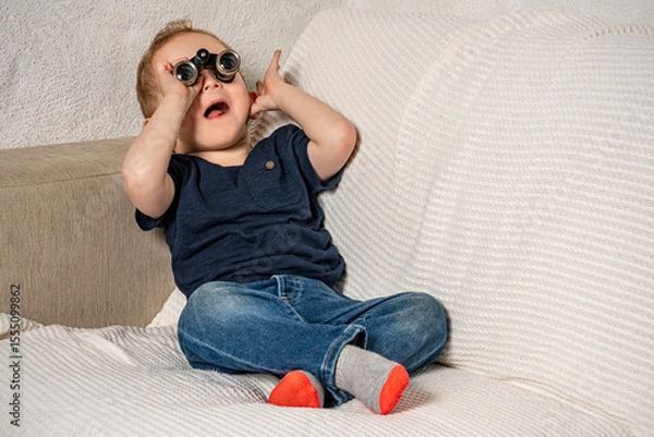 Fototapeta Toddler with tiny binoculars exploring his living room.
Amazed kid discovering his world more closely.