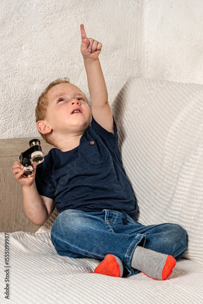 Fototapeta Toddler with tiny binoculars exploring his living room.
Amazed kid discovering his world more closely.