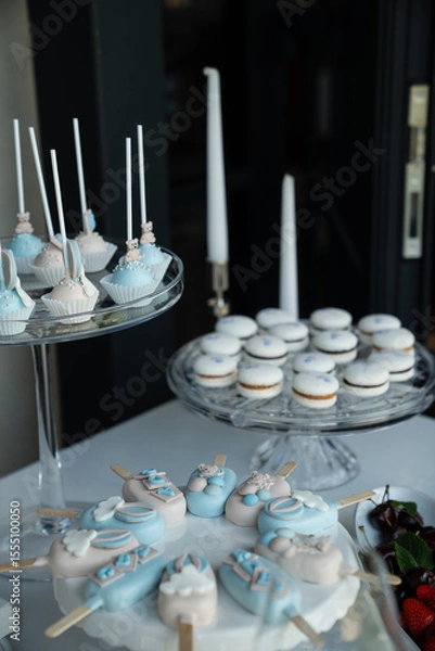Obraz Elegant dessert display with blue and white sweets including cupcakes, macarons, and decorative cake pops for a special occasion.