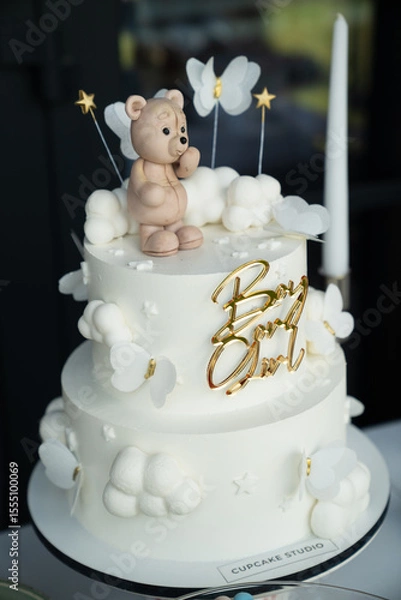Obraz Two-Tiered White Cake with Buttercream, Cloud Decorations, and a Teddy Bear Figurine for a Baby Shower Celebration