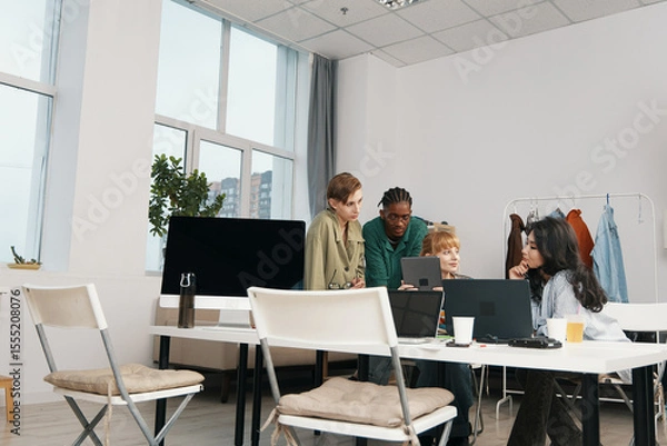 Fototapeta young adult woman and colleagues socializing and working together in a modern workplace, representing Gen Z friends collaborating on business tasks with laptops and digital devices