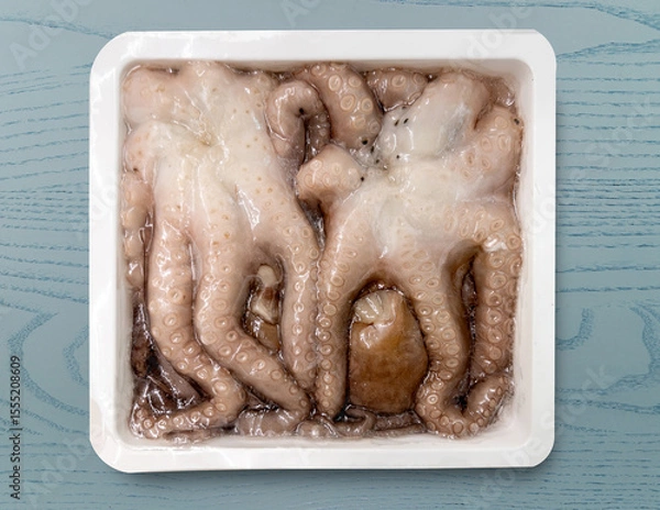 Obraz Vacuum-sealed frozen octopus in  white plastic tray  isolated on blue table with clipping path included