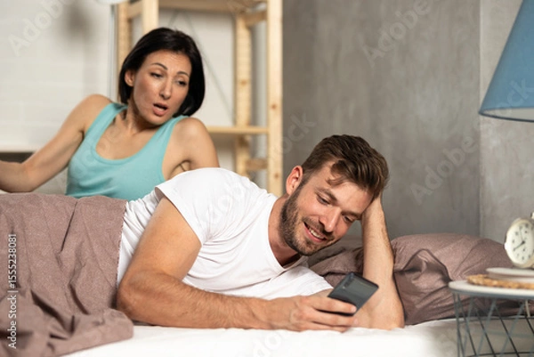 Obraz Cheating husband texting on phone ignoring wife lying in bed.