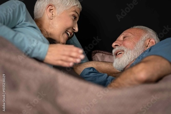 Obraz Smiling senior couple having conversation while lying in bed
