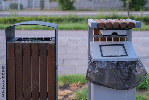 Fototapeta Two public waste bins placed side by side in an urban area, one made of metal and wood, the other featuring a sloped lid and integrated ashtray.