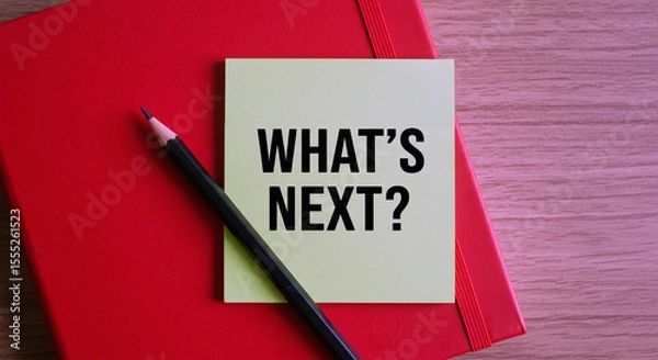 Fototapeta A black pencil rests on a bright red notebook with a light yellow sticky note asking what s next in bold black letters.