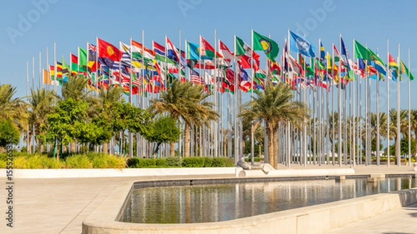 Fototapeta Many world's countries national flags waving on the wind, with UN, EU, GCC, Belarusian, Kyrgyz, Mexican banners with palms and pond in the foreground, Doha, Qatar