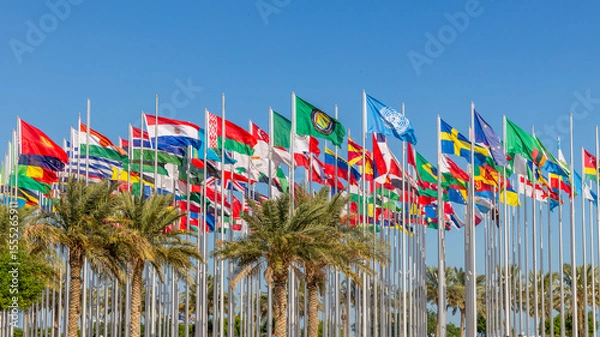 Fototapeta Many world's countries national flags waving on the wind, with UN, EU, GCC, Belarusian, Paraguayan, Mexican banners with palms in the foreground, Doha, Qatar