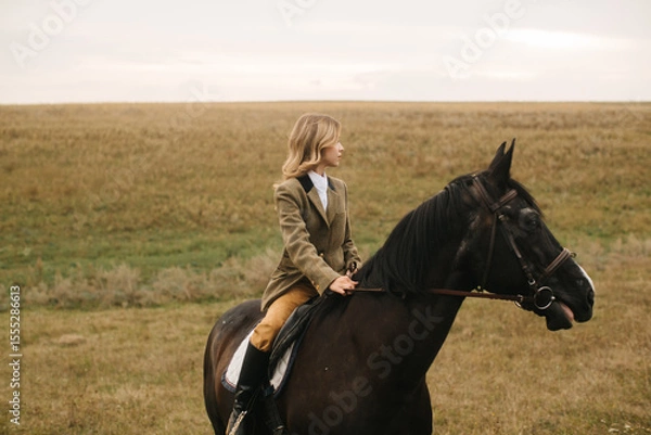 Obraz Young Woman Riding a Black Horse Across a Vast Open Field