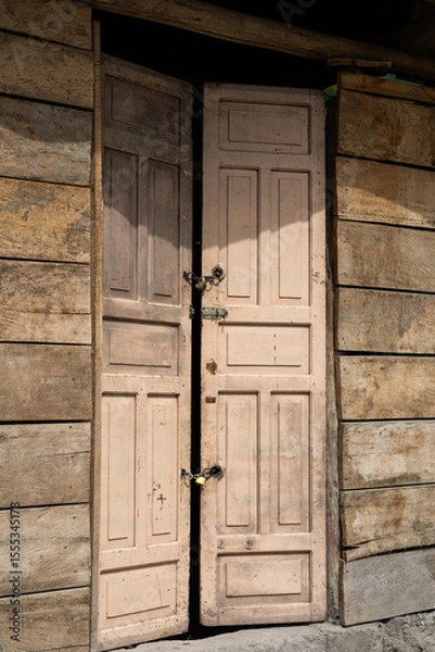 Fototapeta A beautifully aged wooden door stands at the entrance of an old house, rich with texture and character. The rustic design reflects history, craftsmanship, and timeless simplicity.

