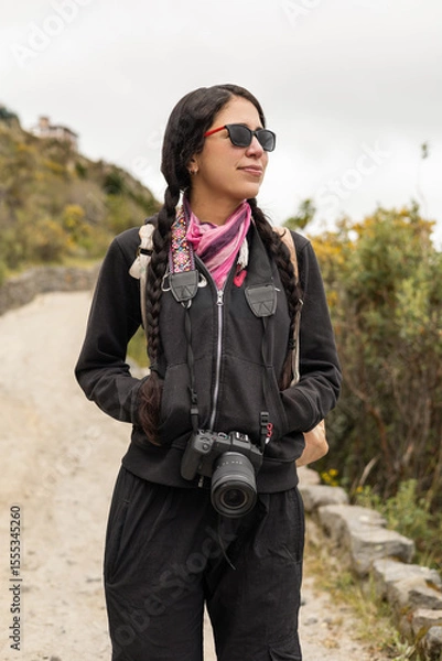 Fototapeta A woman walks along a peaceful dirt trail with her hands in pockets, feeling the cool air. The serene landscape around her adds to the quiet, reflective mood of the moment.

