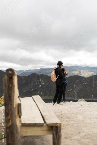 Fototapeta A solitary wooden chair sits near the cliff’s edge while a woman stands in the background, evoking a cinematic and suspenseful atmosphere reminiscent of iconic storytelling moments.

