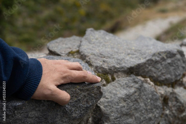 Fototapeta A close-up of a hand gently placed on textured rocks. The image conveys themes of grounding, connection to nature, inner strength, and human presence in the natural world.

