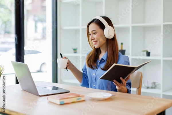 Obraz Focused Smiling girl student wearing headphones taking notes while listening to an online class on her laptop distant education

