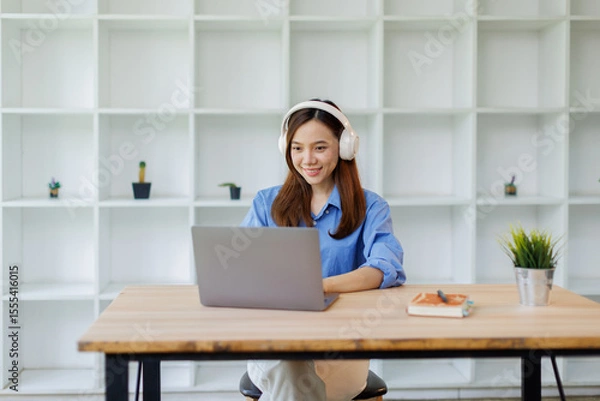 Obraz Beautiful young Asian woman college student wearing white headphones at classroom. College student working on the college campus. back to school concept
