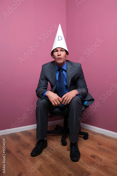 Obraz Businessman sat in corner wearing a dunce hat