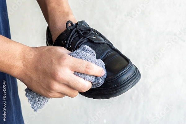 Fototapeta Close-up of hands cleaning and polishing a black leather shoe with a wooden brush. Shoe care, personal grooming, leather maintenance, daily routine concept, isolated on plain background
