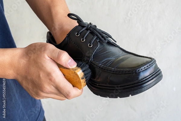 Fototapeta Close-up of hands cleaning and polishing a black leather shoe with a wooden brush. Shoe care, personal grooming, leather maintenance, daily routine concept, isolated on plain background